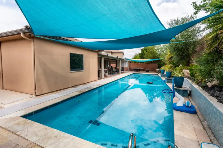 Rectangular swimming pool with light-colored coping, surrounded by a stucco exterior and landscaping