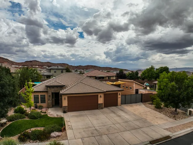 Stone facade accents, tiled roofing, an attached double garage, a concrete driveway, and landscaped front yard with mature plantings