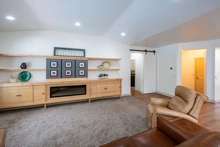 Built-in media console with integrated fireplace, recessed lighting, vaulted ceiling, wood-finish flooring, and barn door access