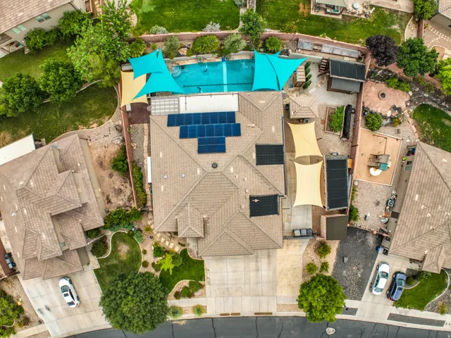 Tiled roof with solar panel arrays, extensive backyard hardscaping, in-ground swimming pool, and multiple shade structures