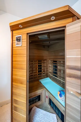 Infrared sauna featuring wood-finish interior paneling, built-in bench seating, control panel with digital display, and glass door with dark-tinted panels for privacy and heat retention