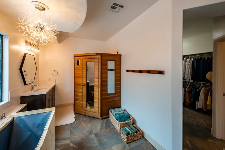 Stone-finish flooring, wood-paneled sauna, vanity with single sink and counter space, decorative light fixture, and walk-in closet with shelving