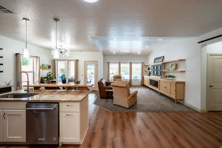 Open-concept interior featuring wood-finish flooring, a kitchen island with stone countertops, stainless steel appliances, and recessed lighting