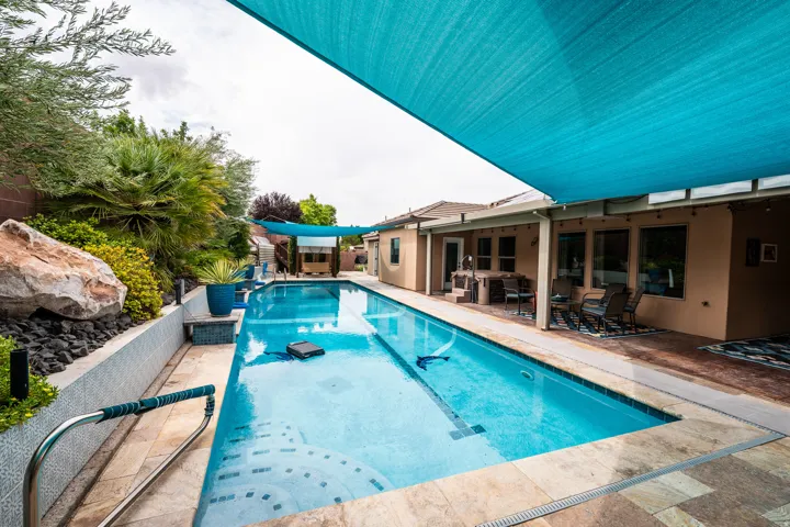 Elongated swimming pool with integrated sun shade, tiled retaining wall, and surrounding hardscaping