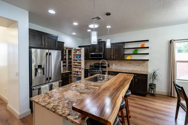 Gourmet kitchen featuring stainless steel appliances, dual-tone cabinetry with dark wood finishes, stone countertops with waterfall edge, pendant lighting, and a wood-finish island with seating for multiple guests