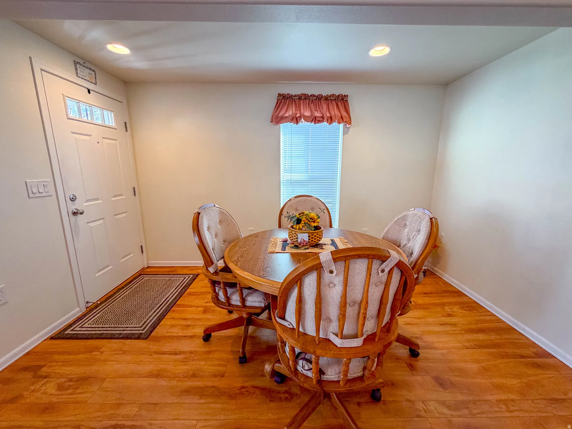 Wood-finish flooring throughout, recessed ceiling lighting, a white entry door with a clear glass insert, and a window with blinds