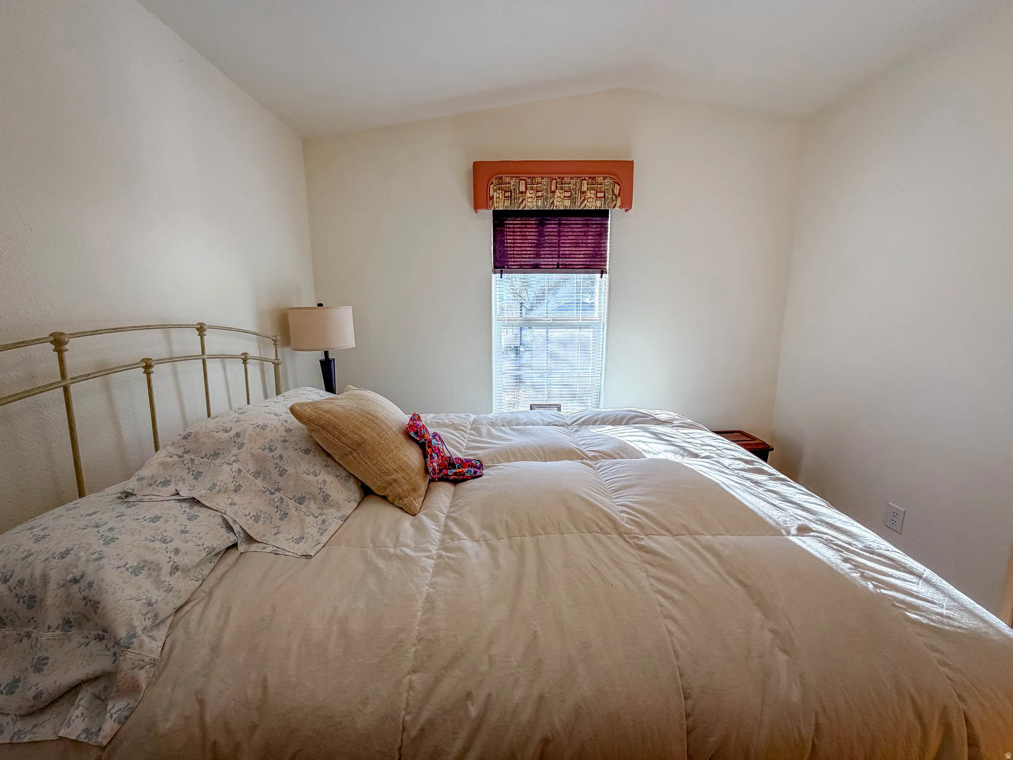 Vaulted ceiling, window with blinds, wall-mounted light fixture, and light-toned walls