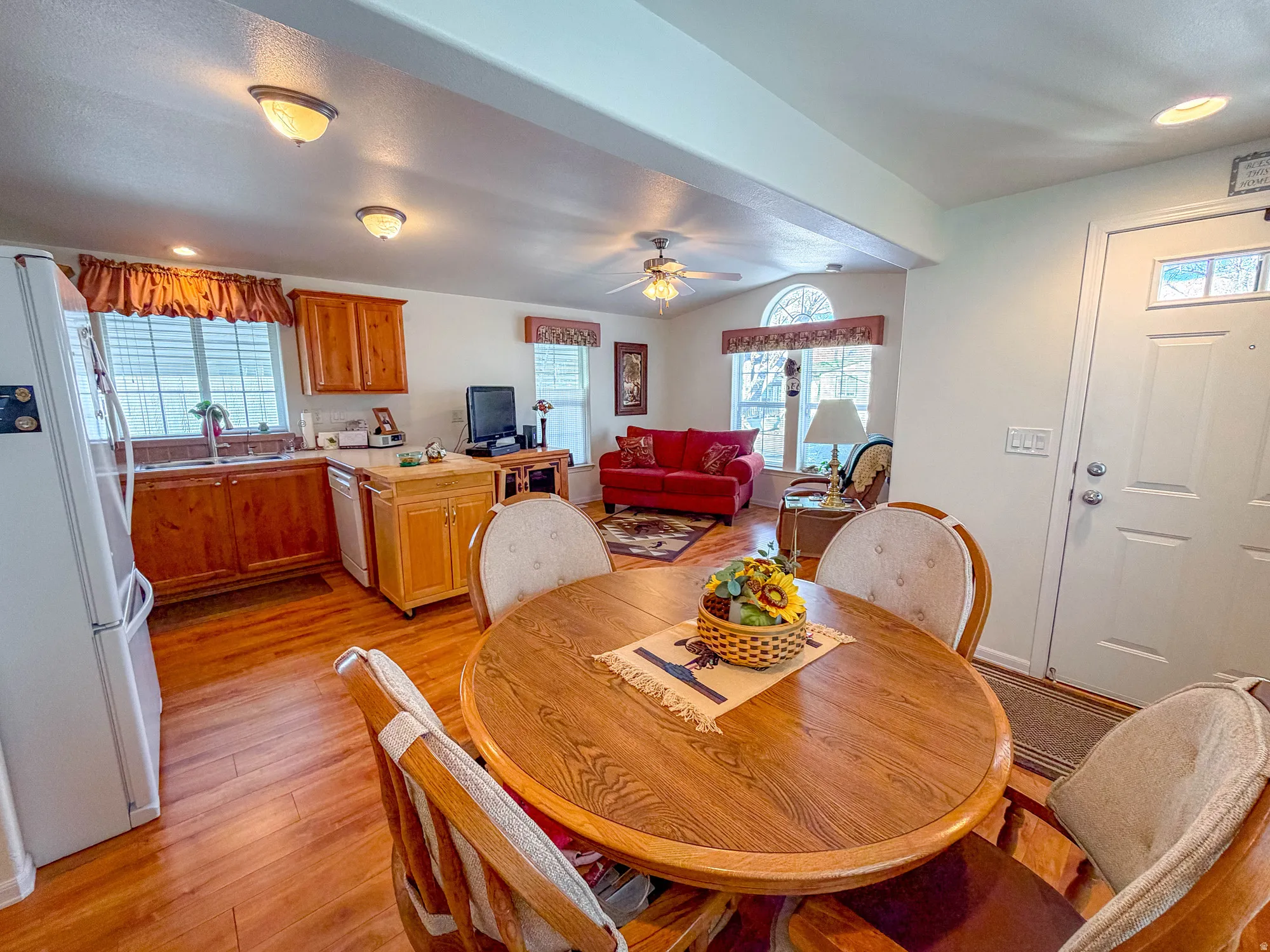 Wood-finish flooring throughout, kitchen with wood cabinetry and stainless steel sink, recessed lighting and ceiling fan, and a front entry door with decorative glass