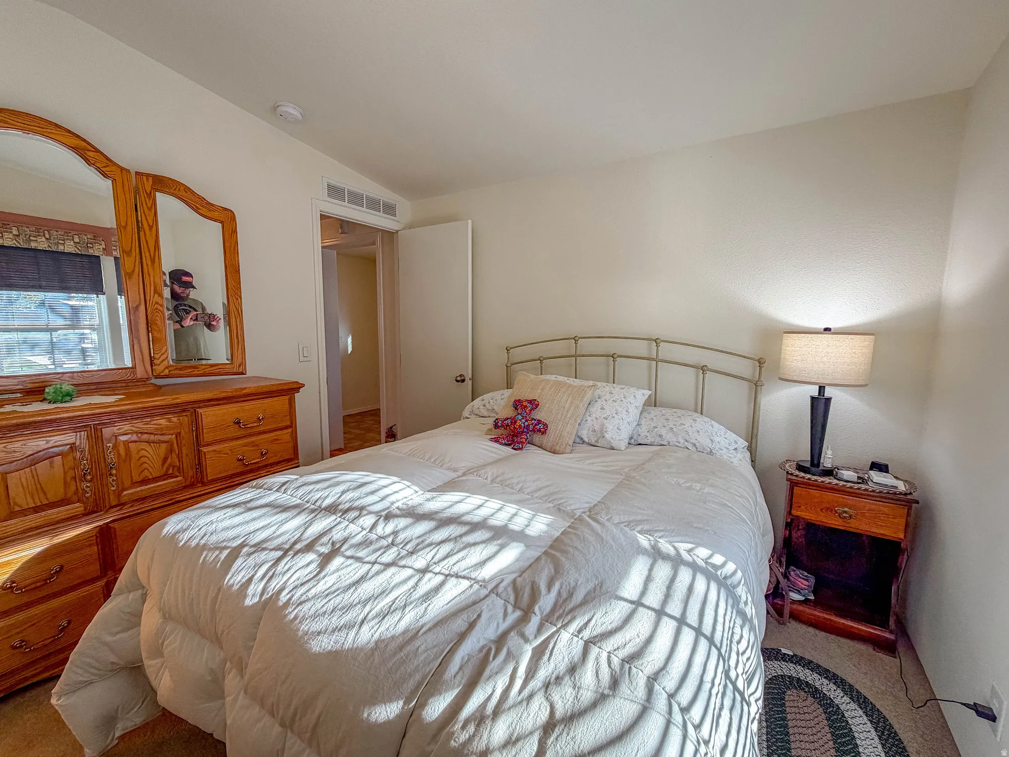 Neutral wall paint, window with roller shade, and warm-toned wood-finish dresser with attached mirrors