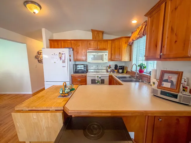Kitchen featuring wood cabinetry, laminate countertops, a white refrigerator, a double basin sink, and wood-finish flooring