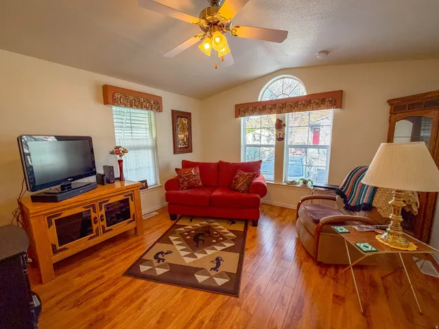 Vaulted ceiling, wood-finish flooring, ceiling fan with integrated lighting, multiple windows with blinds, and an arched transom window