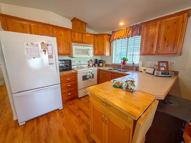 Wood-finish flooring, wood cabinetry, white appliances, double basin sink, and a built-in island with countertop