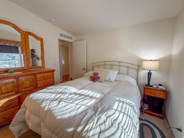 Neutral wall paint, window with roller shade, and warm-toned wood-finish dresser with attached mirrors