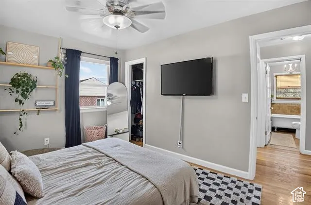 Ceiling fan light fixture, window with dark drapes, wood-finish flooring, built-in shelving, and a wall-mounted display