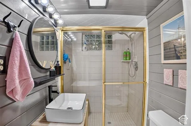 Bathroom featuring shiplap wall paneling, a vessel sink, a shower with glass block accents, and a gold-finish shower enclosure