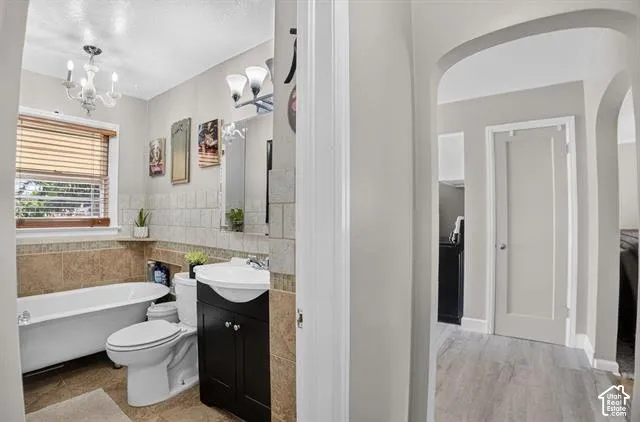 Bathroom featuring a clawfoot tub, tile wainscoting, a dark wood-finish vanity, and a chandelier