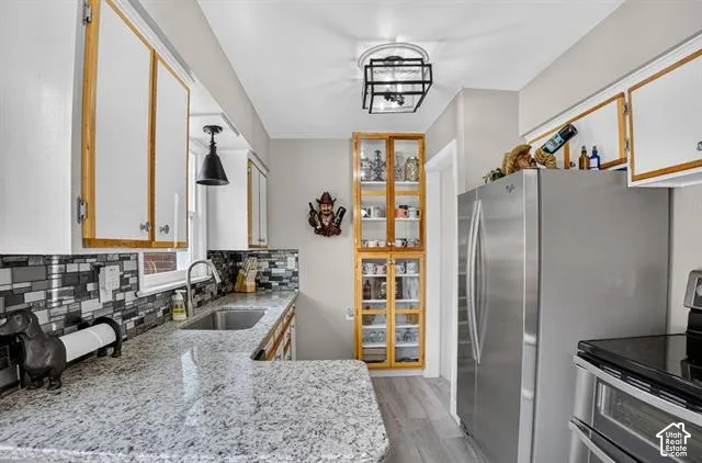 Galley kitchen featuring granite-style countertops, mosaic tile backsplash, stainless steel refrigerator, wood-finish flooring, and a built-in display cabinet