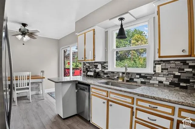 Kitchen featuring wood-finish flooring, granite-style countertops, a mosaic tile backsplash, white cabinetry with wood trim, and a stainless steel sink
