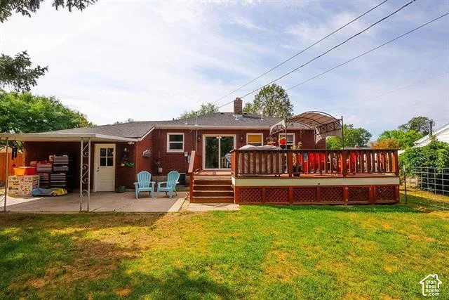 Expansive backyard featuring a brick exterior, covered patio, wood-finish deck with railing, and a sliding glass door