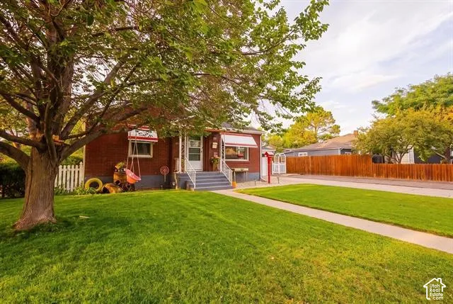 Brick exterior with white awnings, mature front yard tree, picket fence, and a concrete walkway