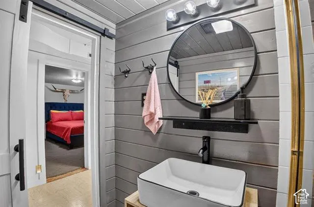 Modern bathroom featuring shiplap accent wall, circular framed mirror with integrated shelf, rectangular vessel sink with matte black faucet, and vanity lighting