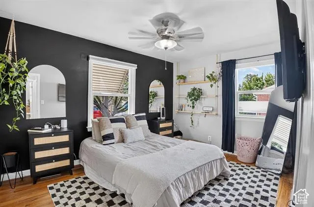 Hardwood flooring, two windows with blinds, ceiling fan with integrated lighting, built-in shelving, arched wall mirrors