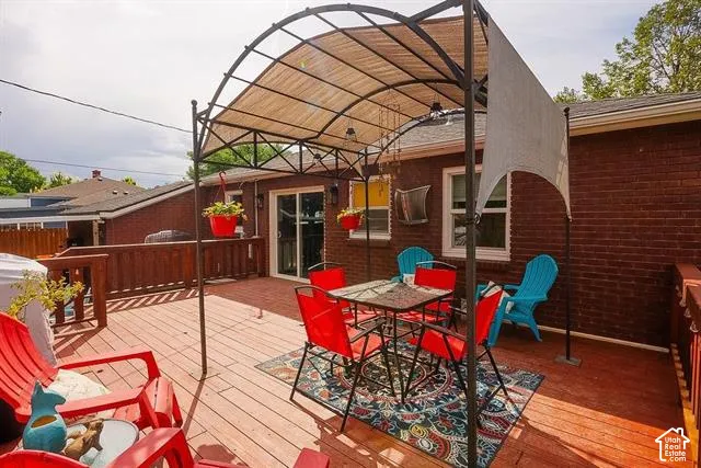 Expansive wood deck with a privacy screen, metal pergola, sliding glass door, and brick exterior