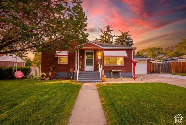 Charming red brick residence featuring a welcoming front entrance with illuminated windows, concrete walkway, and manicured lawn