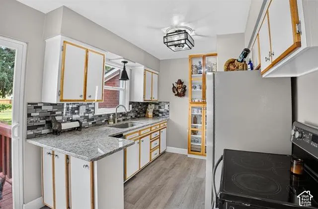 Kitchen featuring wood-finish flooring, white cabinetry with wood trim, gray speckled countertops, a mosaic tile backsplash, and a stainless steel sink with an attached faucet