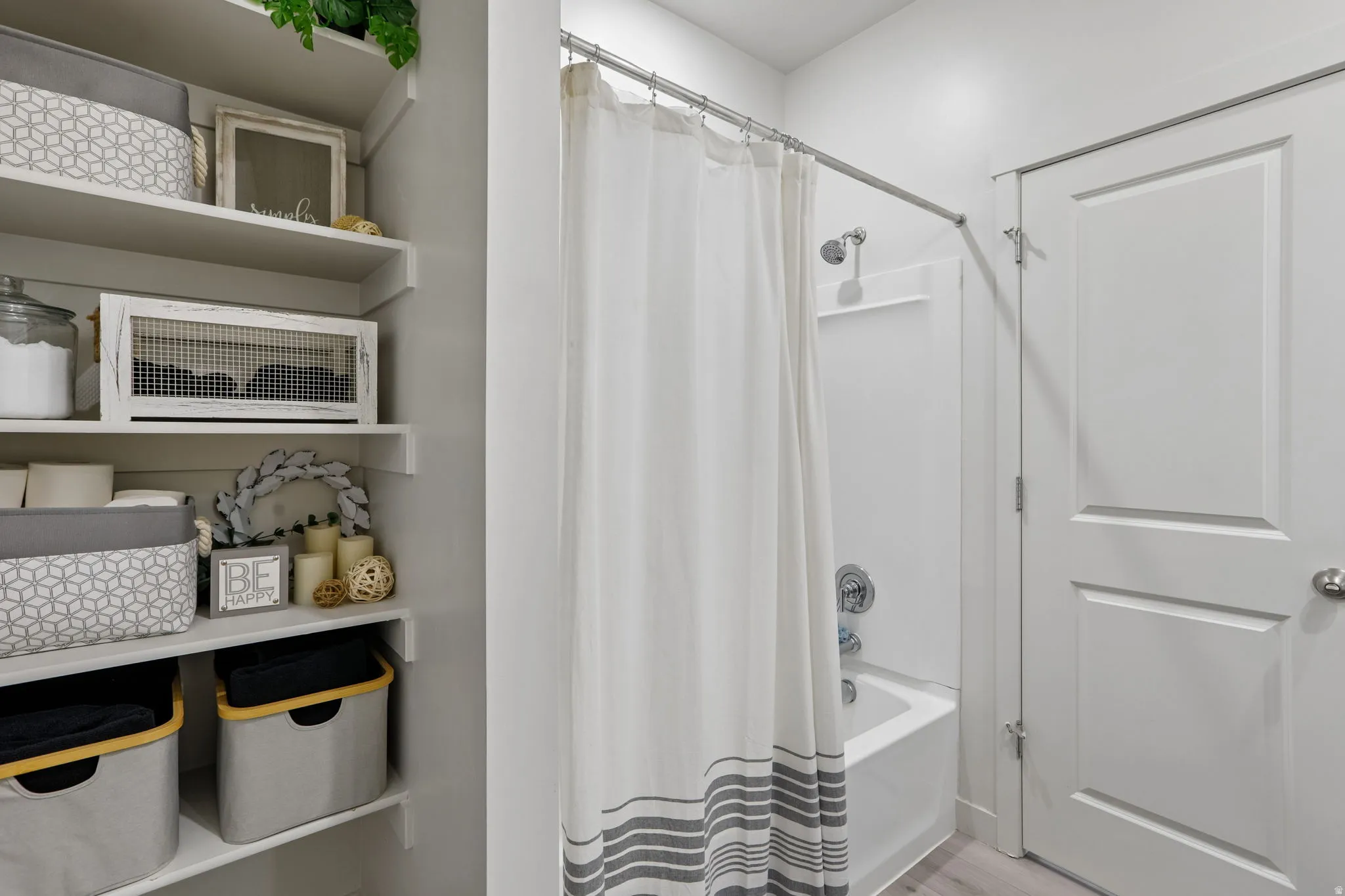 Built-in shelving for organized storage, white paneled door, and a shower-over-tub combination with a chrome shower head and fixtures