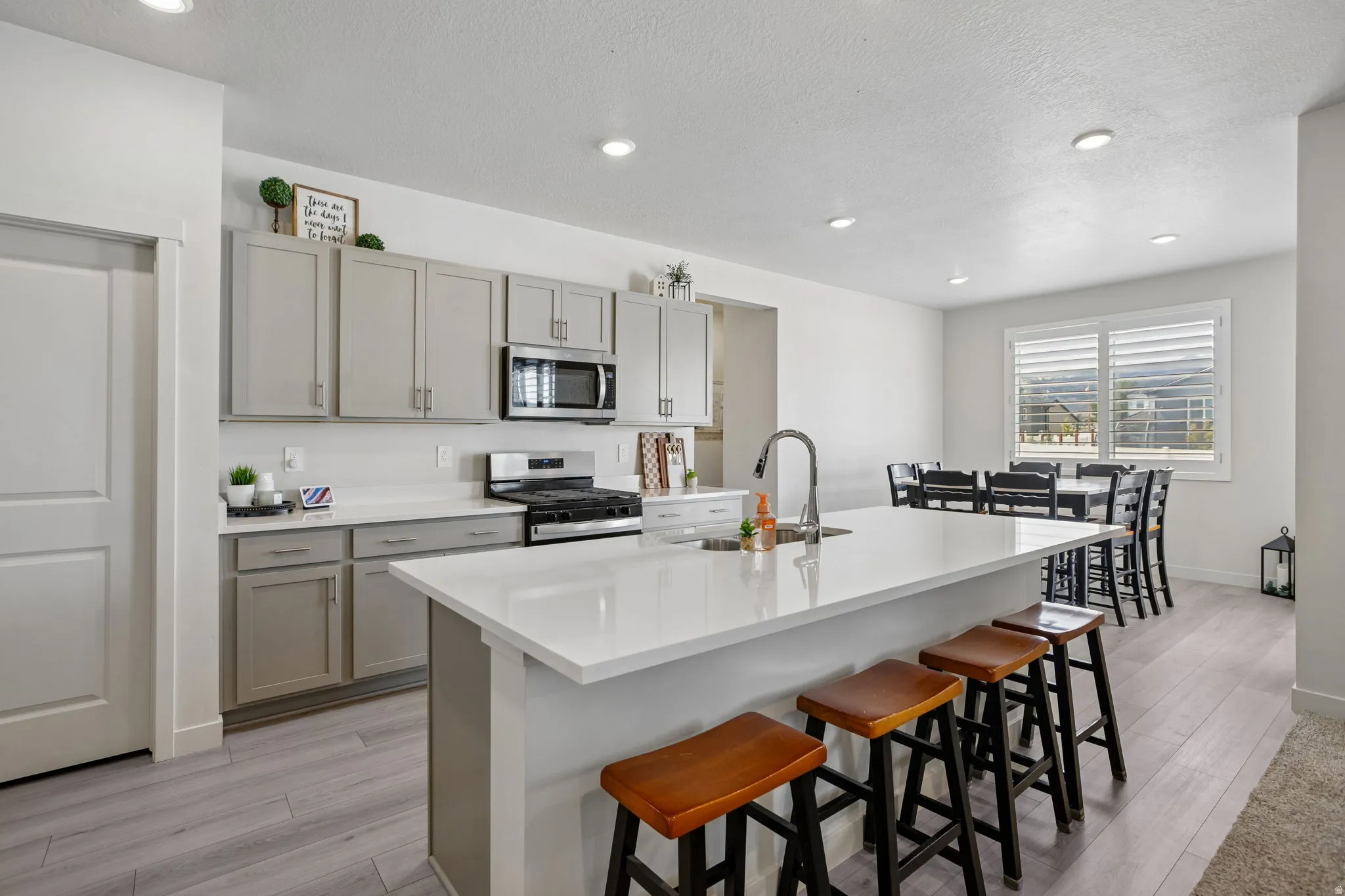 Kitchen featuring a large island with white countertops, stainless steel appliances, light gray cabinetry, recessed lighting, and wood-finish flooring