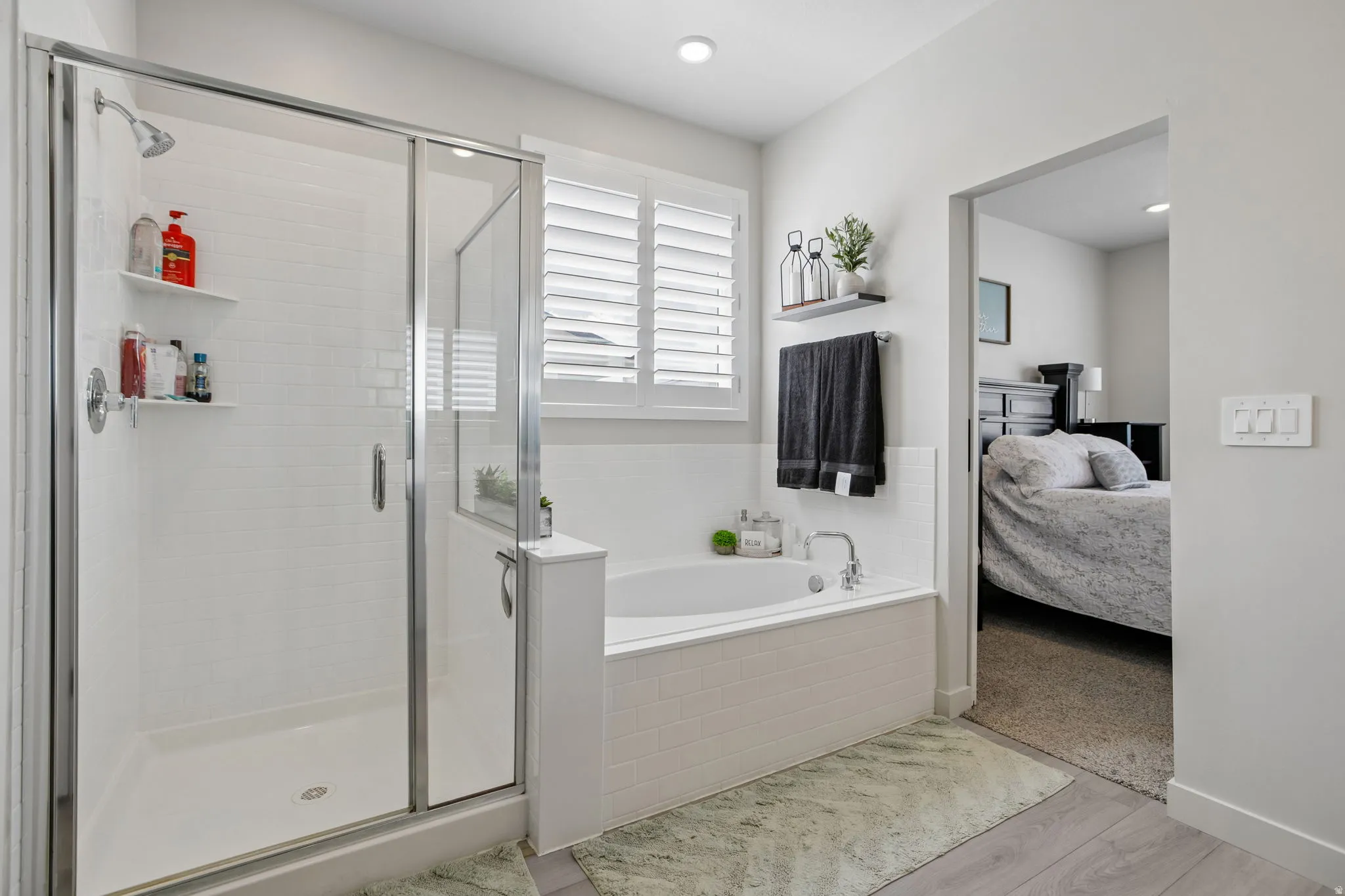 Walk-in shower with clear glass enclosure and white subway tile surround, separate soaking tub with white tile surround, white window shutters, and recessed lighting