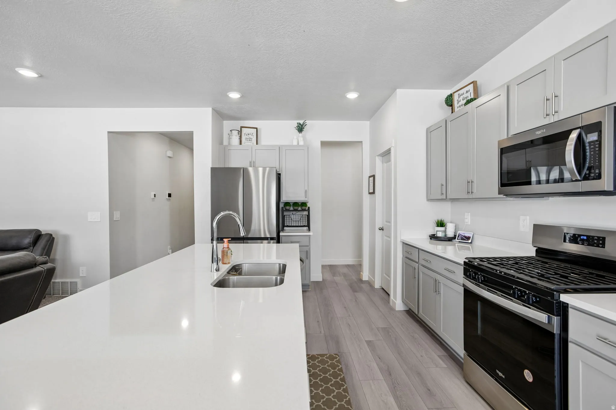 Kitchen with a large island featuring a dual-basin sink, light-toned cabinetry, stainless steel appliances, and wood-finish flooring