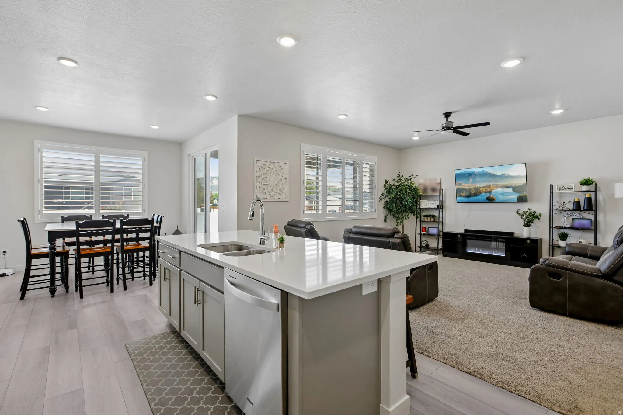 Open-concept living space featuring an island kitchen with a stainless steel sink, a dining area, and a living area with recessed lighting