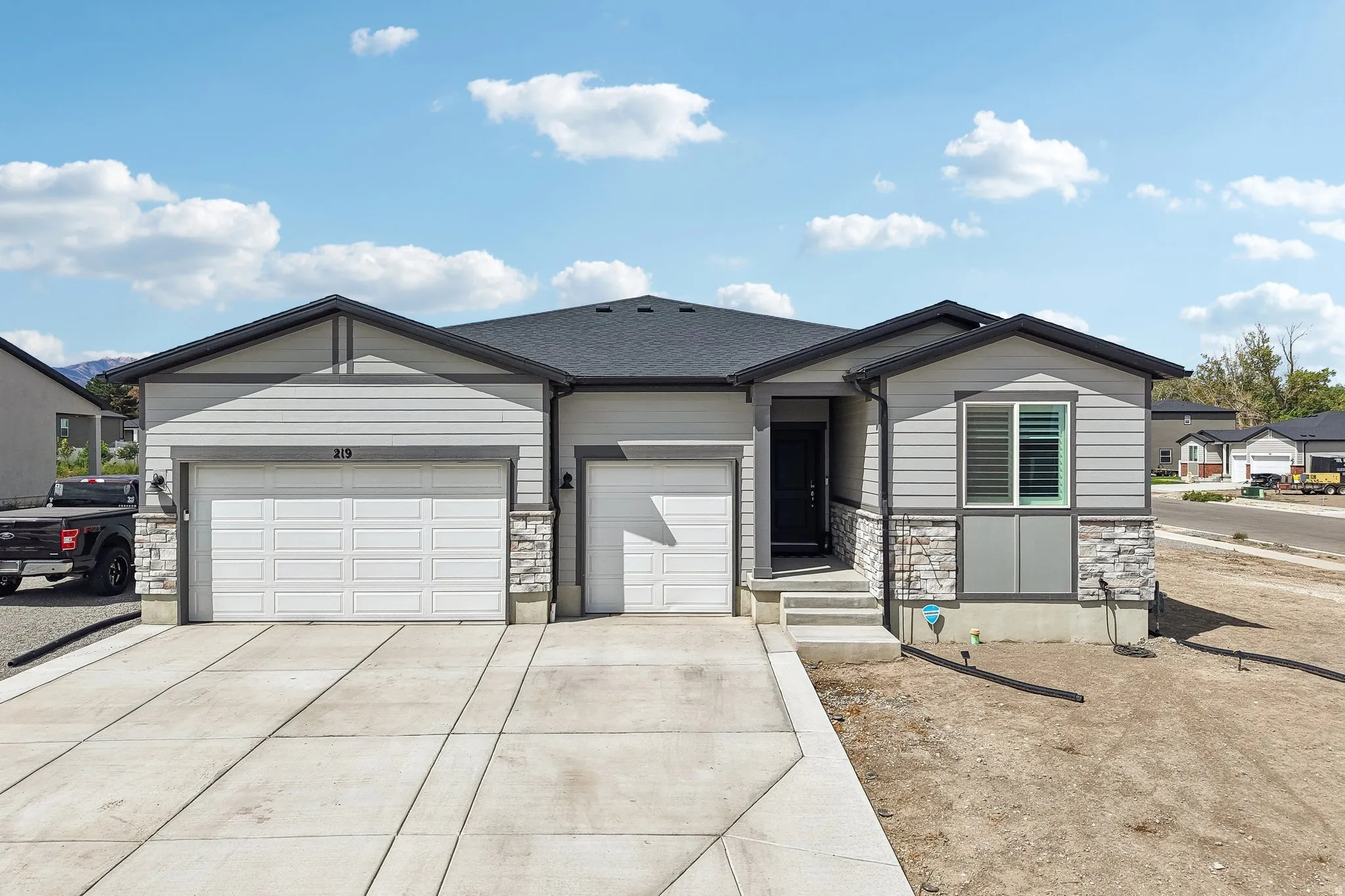 Contemporary exterior with light gray siding, dark trim, stone accents, and a two-car garage