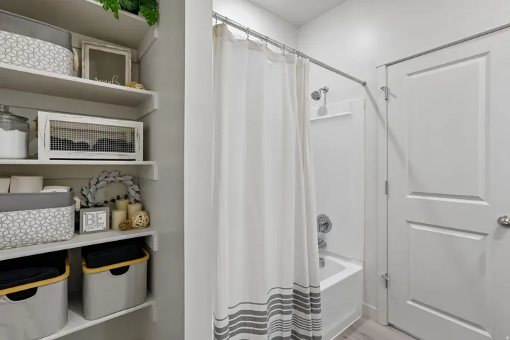 Built-in shelving for organized storage, white paneled door, and a shower-over-tub combination with a chrome shower head and fixtures