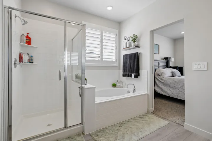 Walk-in shower with clear glass enclosure and white subway tile surround, separate soaking tub with white tile surround, white window shutters, and recessed lighting