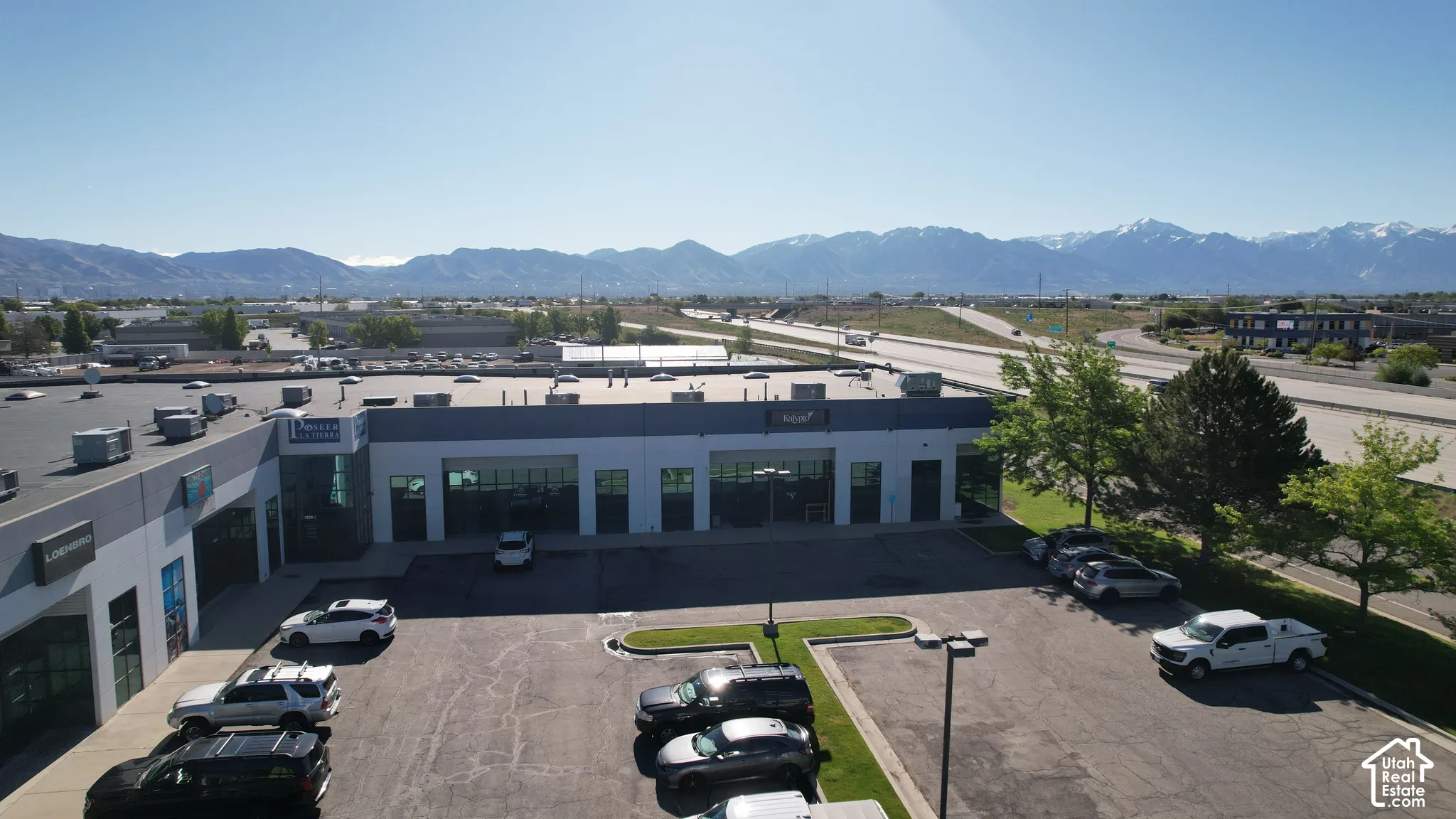 Commercial building with a paved parking lot, adjacent green space, and a mountainous backdrop