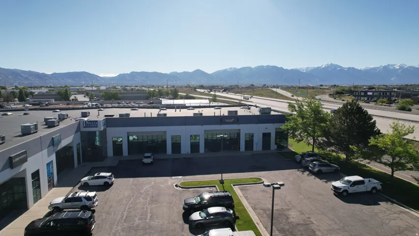 Commercial building with a paved parking lot, adjacent green space, and a mountainous backdrop