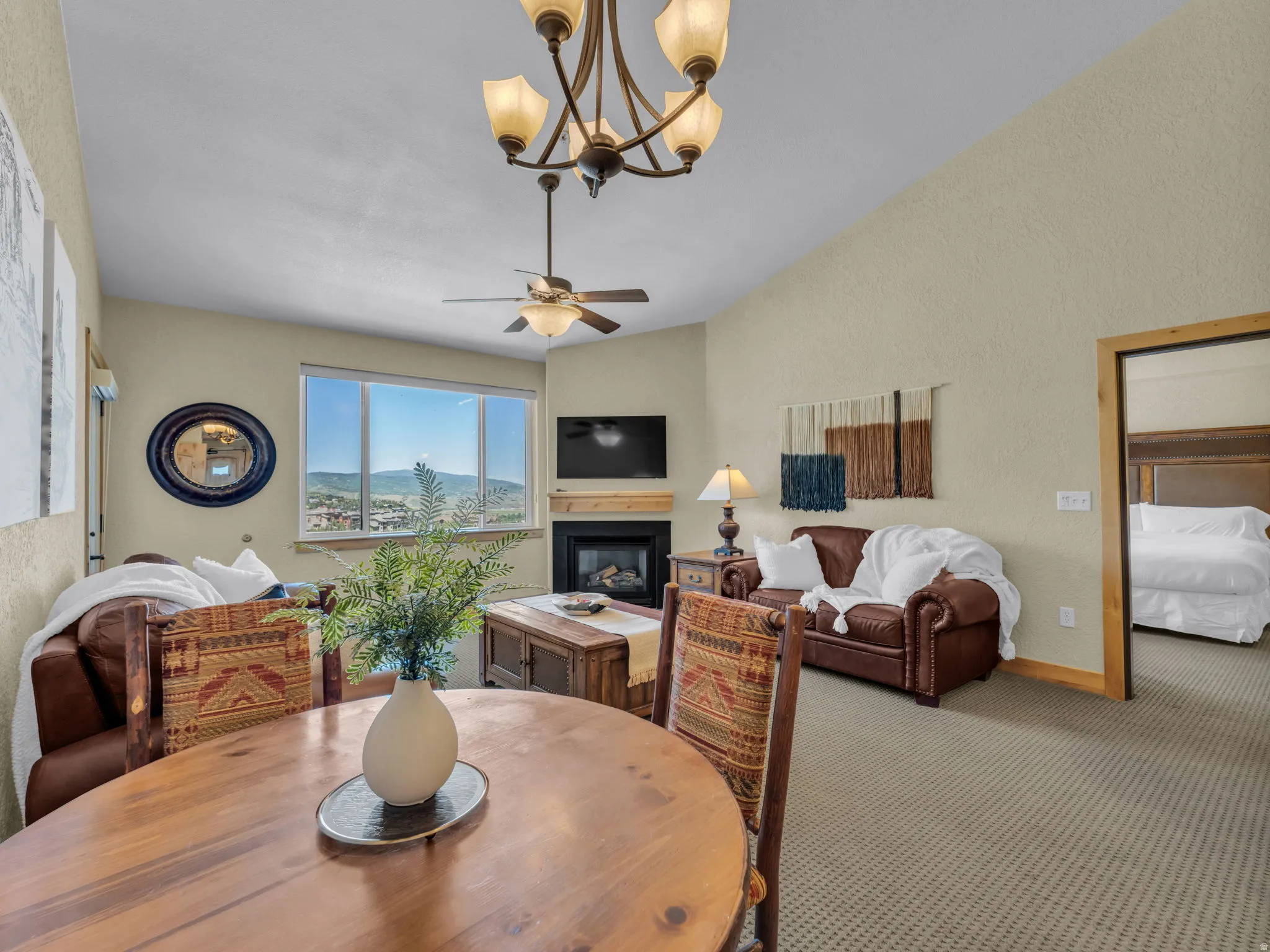 Vaulted ceilings with a chandelier, large windows, a fireplace with a wood mantle, and wood-finish flooring
