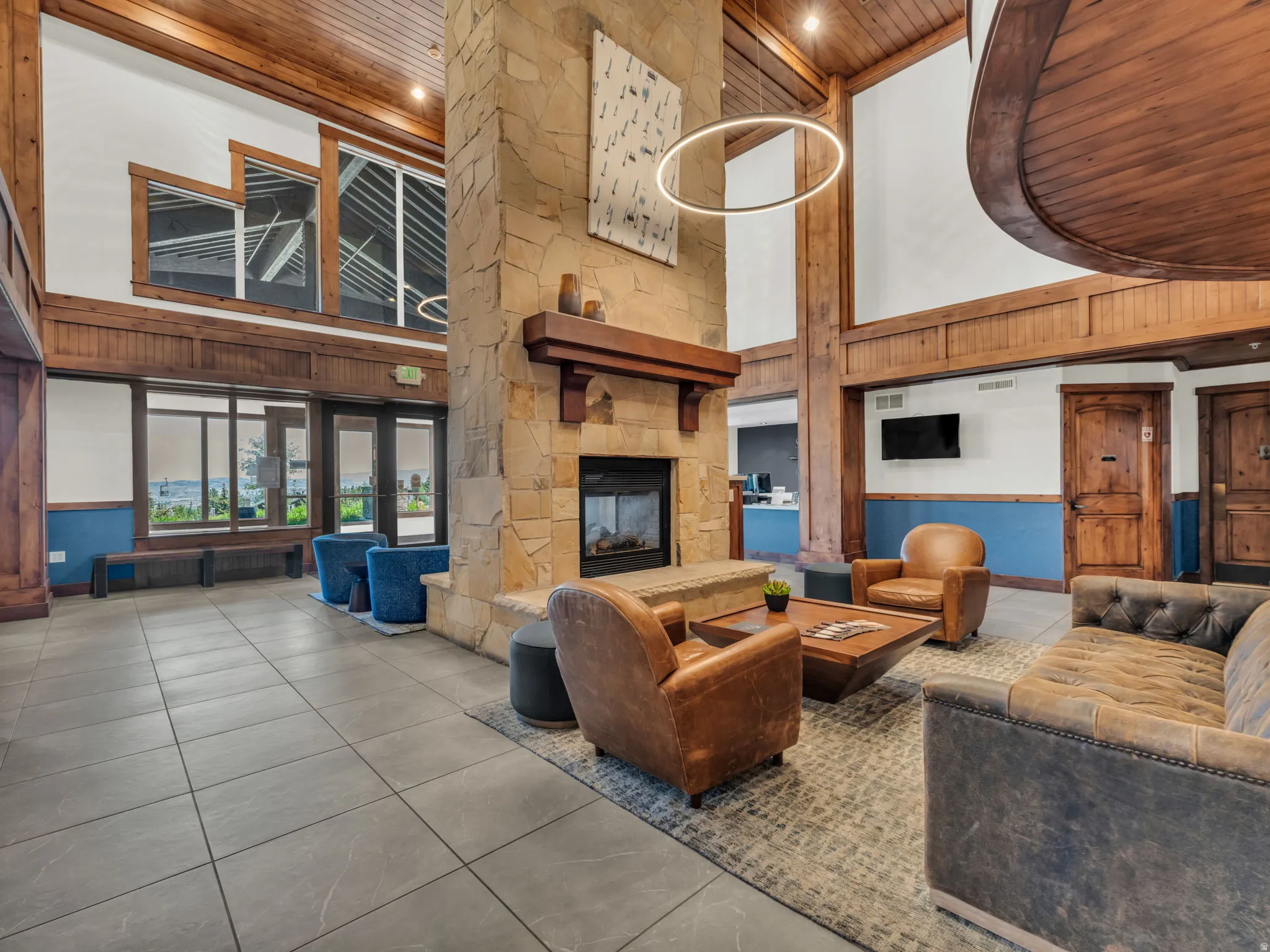 Great room featuring a floor-to-ceiling stone fireplace, soaring wood-paneled ceilings, and large format tile flooring