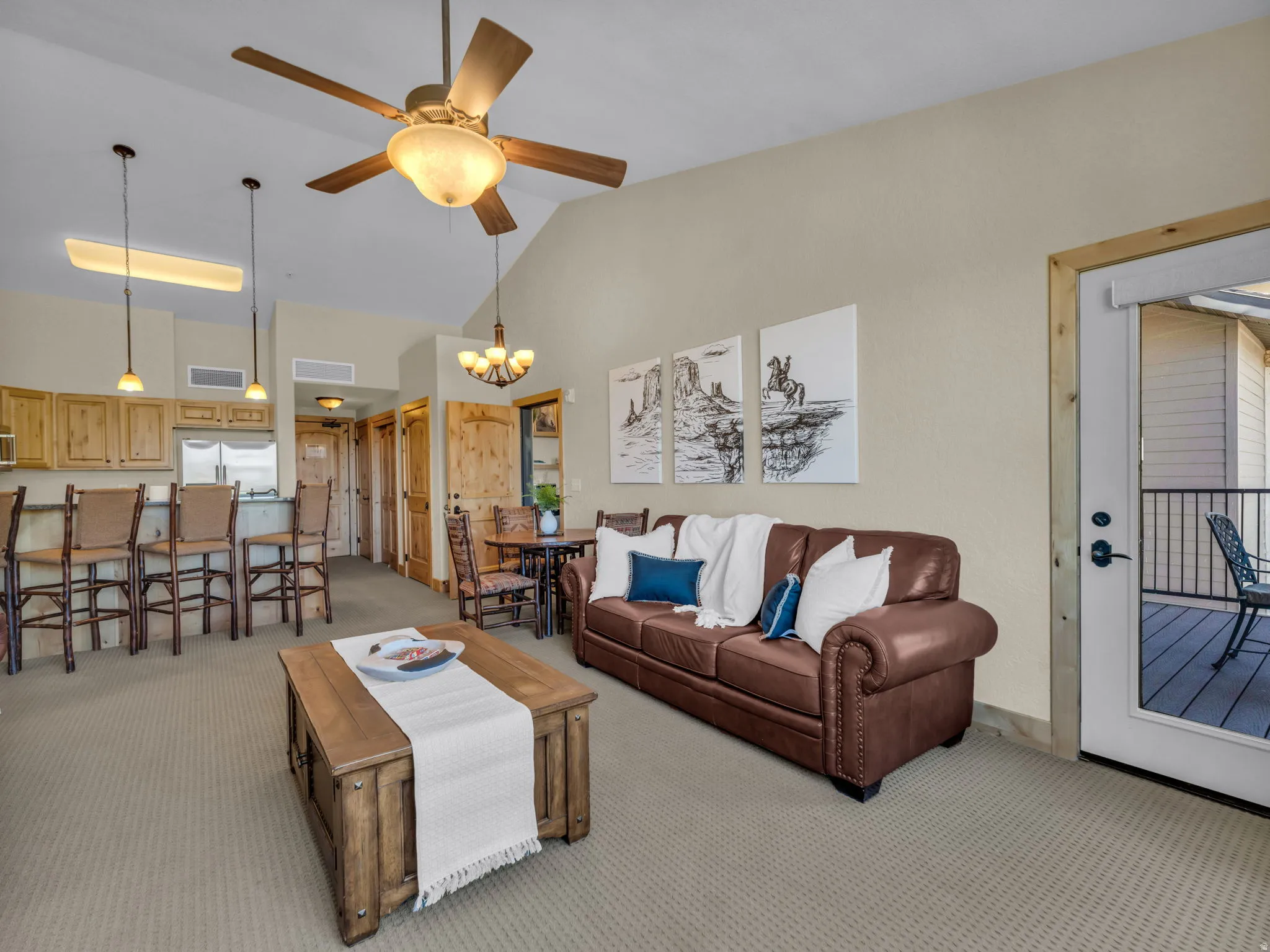 Vaulted ceiling with ceiling fan, kitchen with wood cabinetry and stainless steel appliances, breakfast bar, and outdoor balcony access