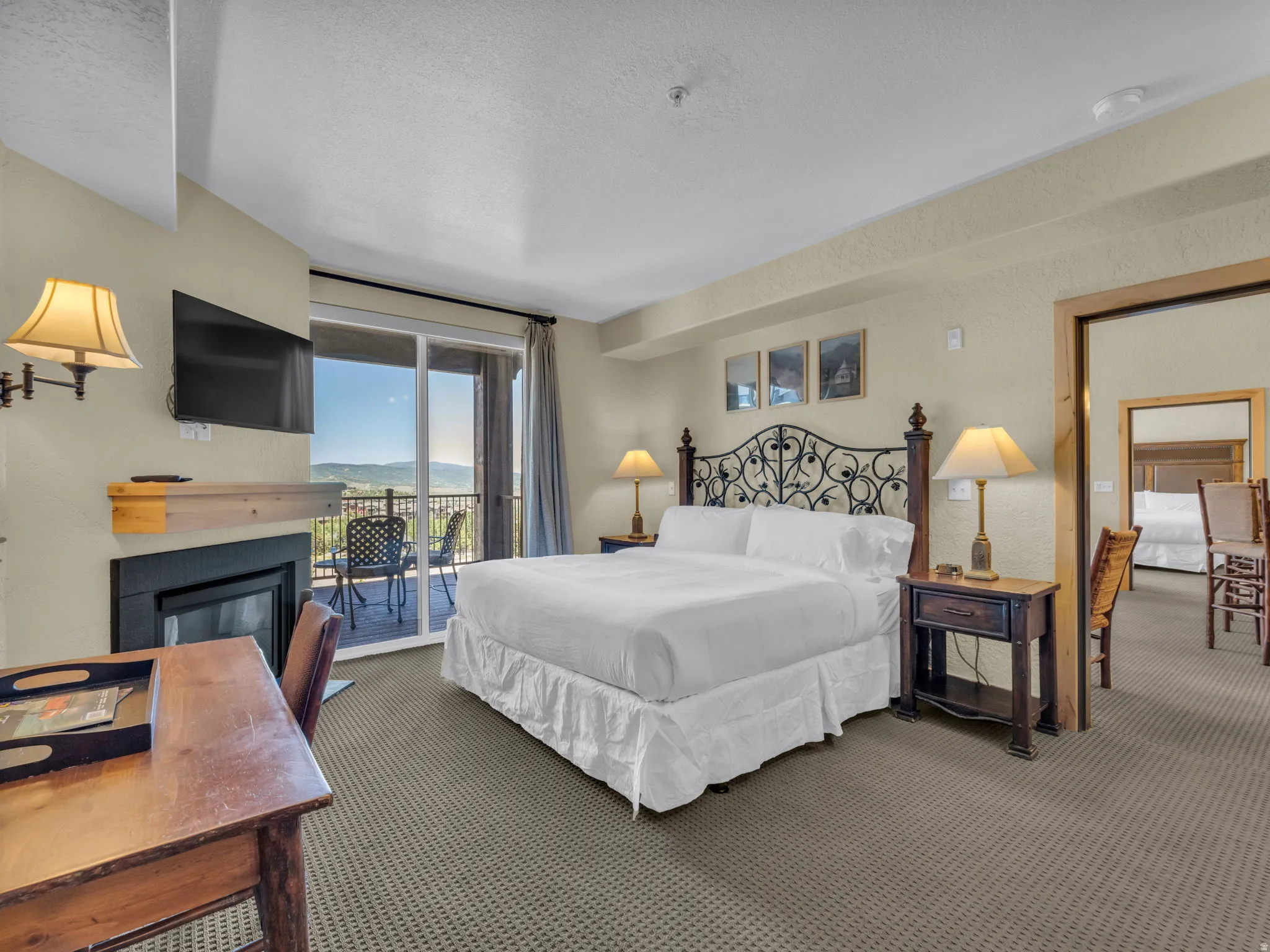 Private balcony, built-in fireplace with wood mantel, sliding glass door, textured carpet flooring, and a wrought iron headboard