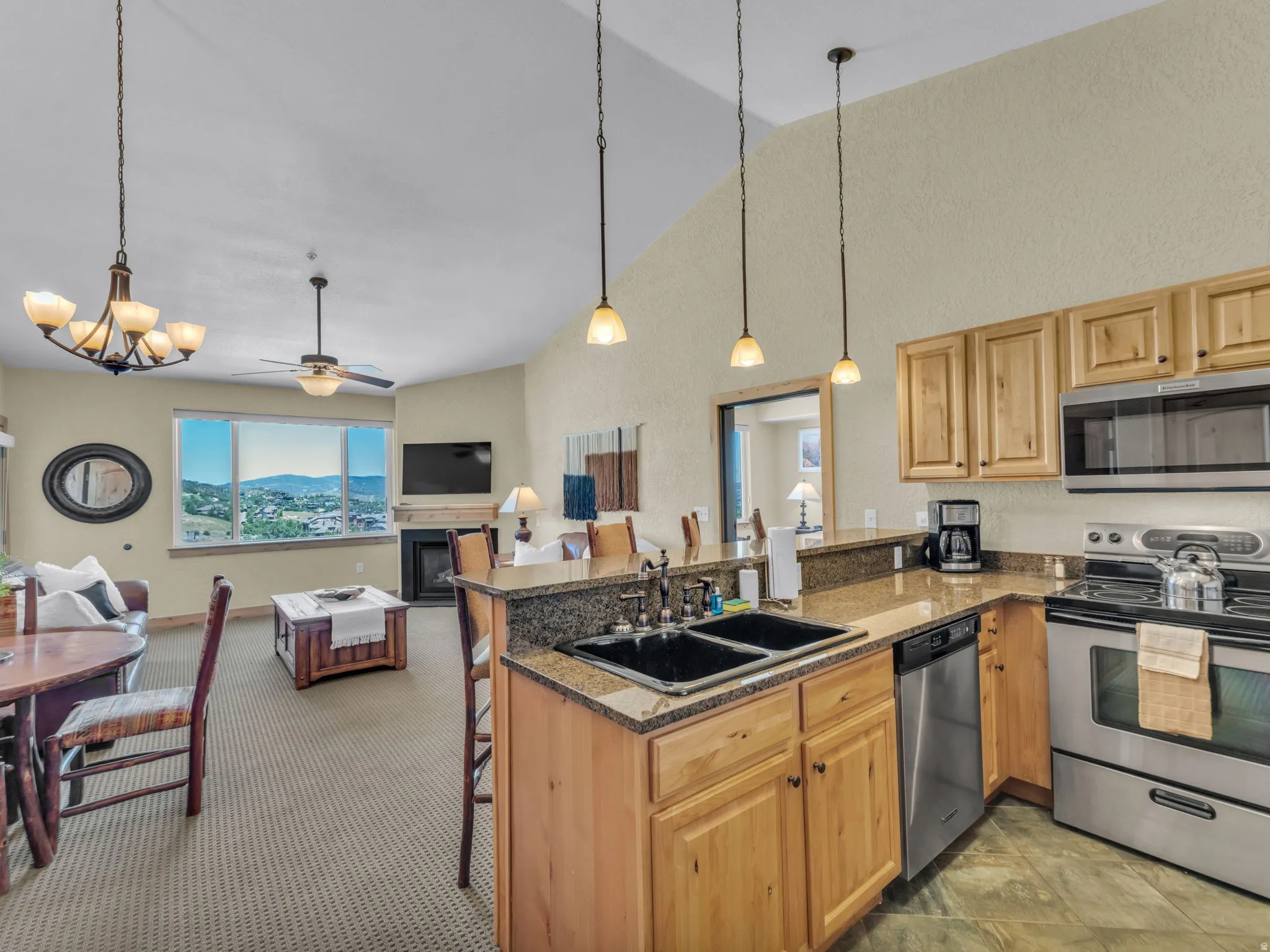 Open-concept living area with vaulted ceilings, a fireplace, and a kitchen featuring wood cabinetry, stone countertops, and stainless steel appliances