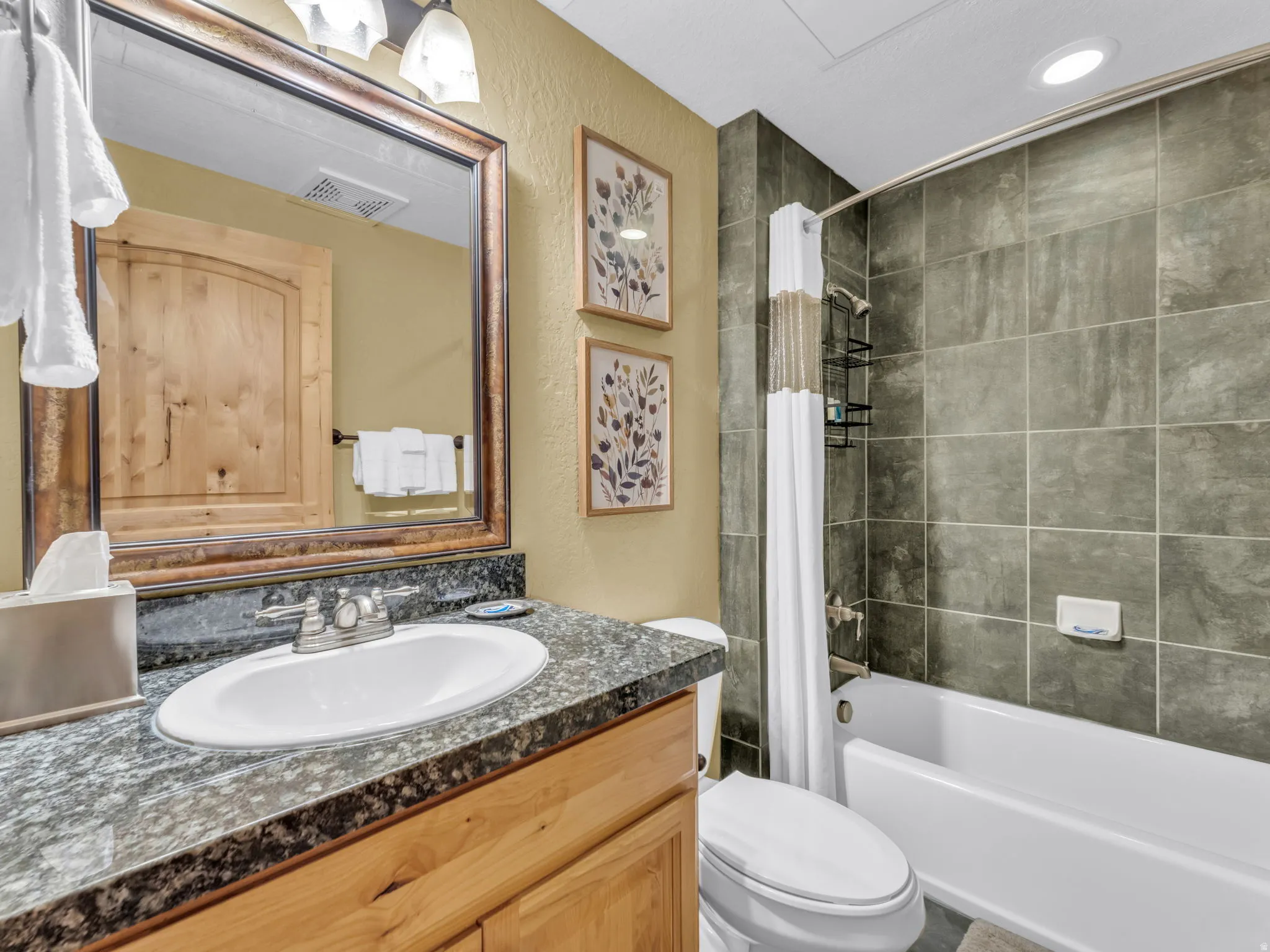 Bathroom featuring a vanity with an undermount sink, speckled countertop, wood-finish cabinetry, a framed mirror, and a tiled tub/shower combination