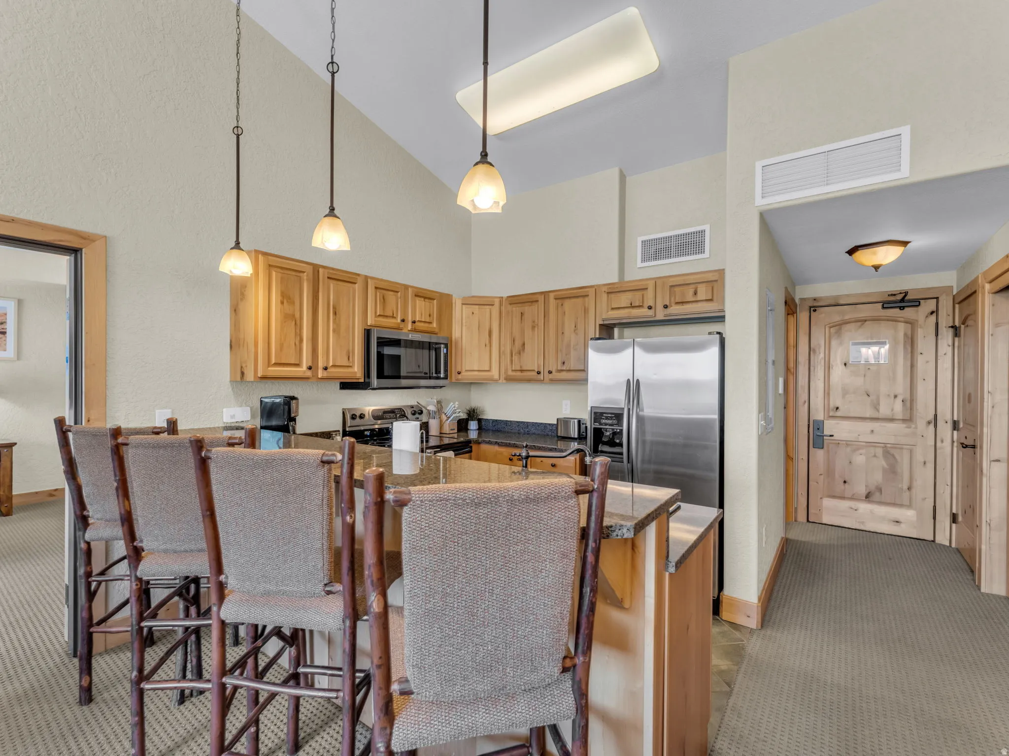 Vaulted ceiling kitchen featuring wood cabinetry, stainless steel appliances, granite countertops, and a breakfast bar