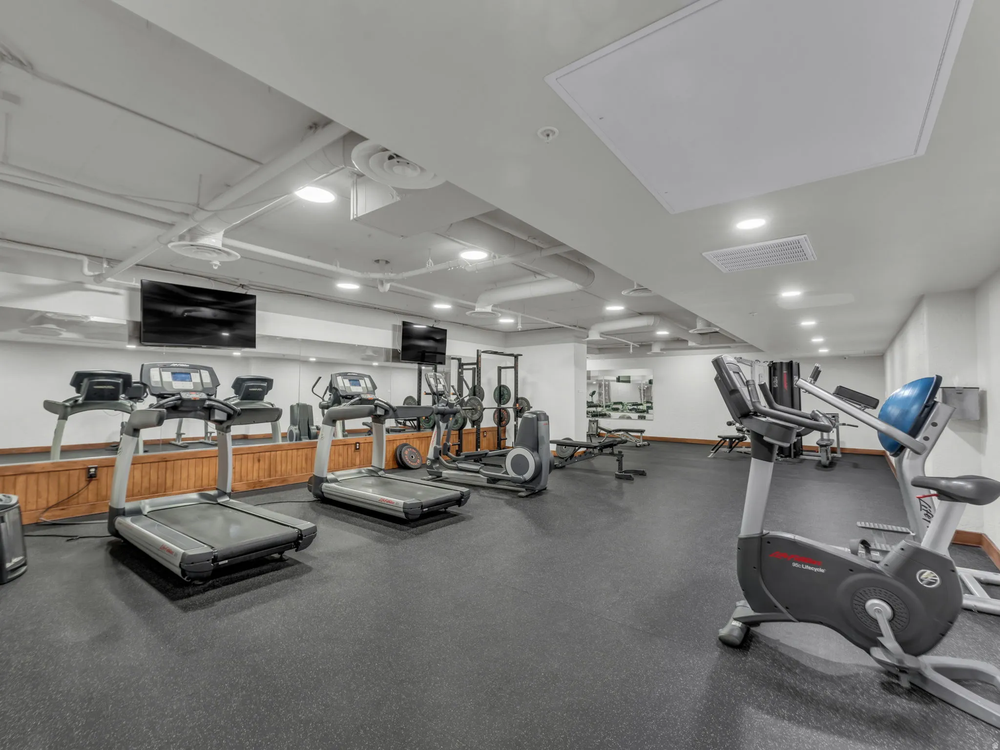 Fitness room featuring rubber flooring, mirrored walls, recessed lighting, and wall-mounted televisions