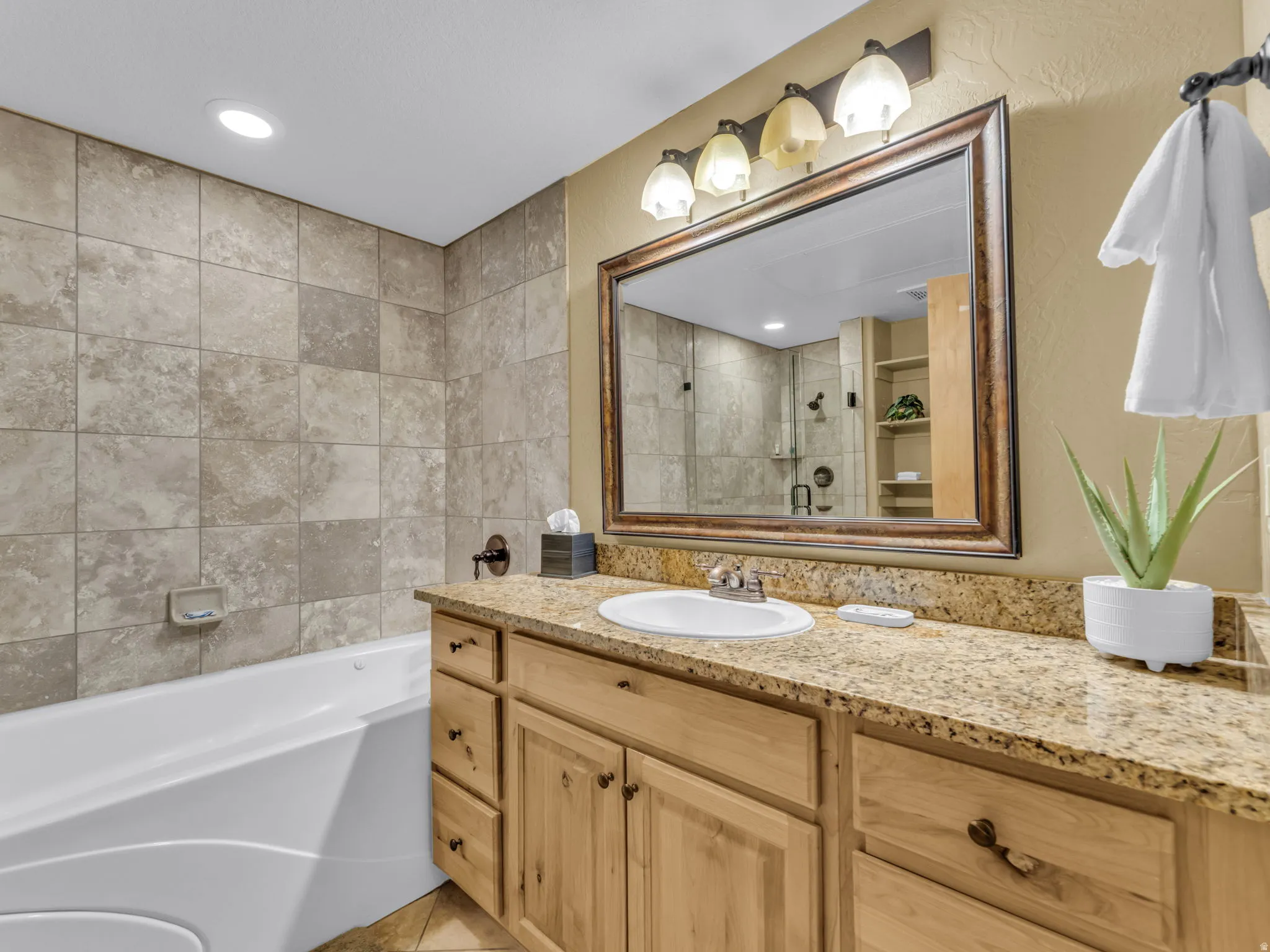 Bathroom featuring a built-in tub, tiled shower surround, a wood-finish vanity with a stone countertop, and an integrated sink