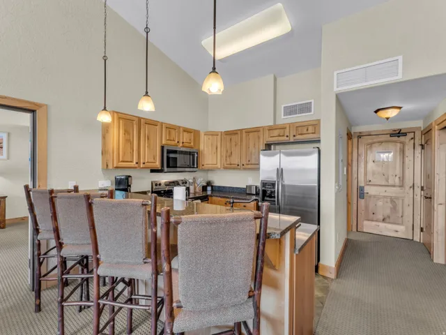 Vaulted ceiling kitchen featuring wood cabinetry, stainless steel appliances, granite countertops, and a breakfast bar