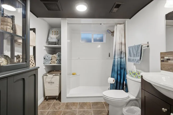 Bathroom with tile flooring, dark wood-finish vanity, integrated sink, and white shower surround with a window